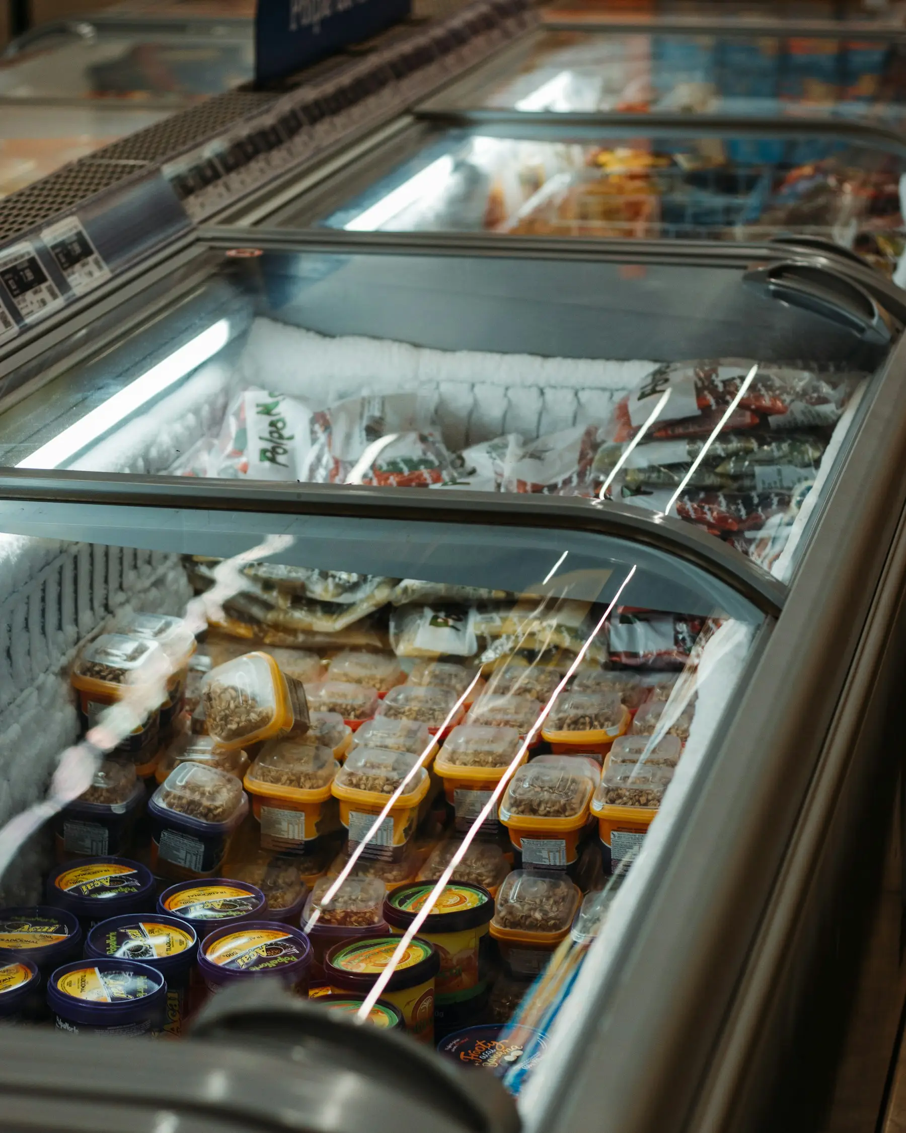 Frozen food in tubs and bags inside a glass-topped supermarket freezer