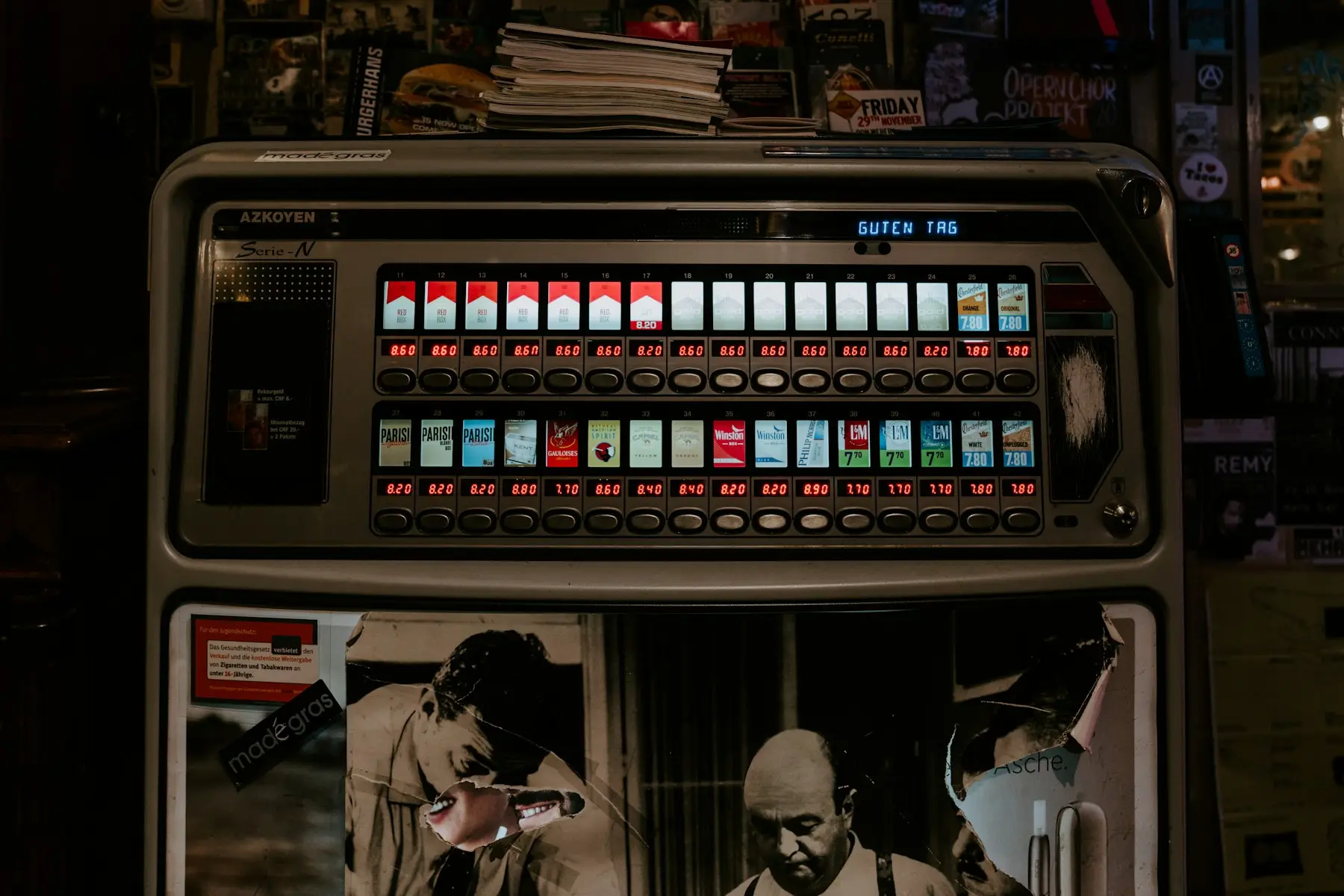 A cigarette vending machine inside a bar, with a lit price under each pack
