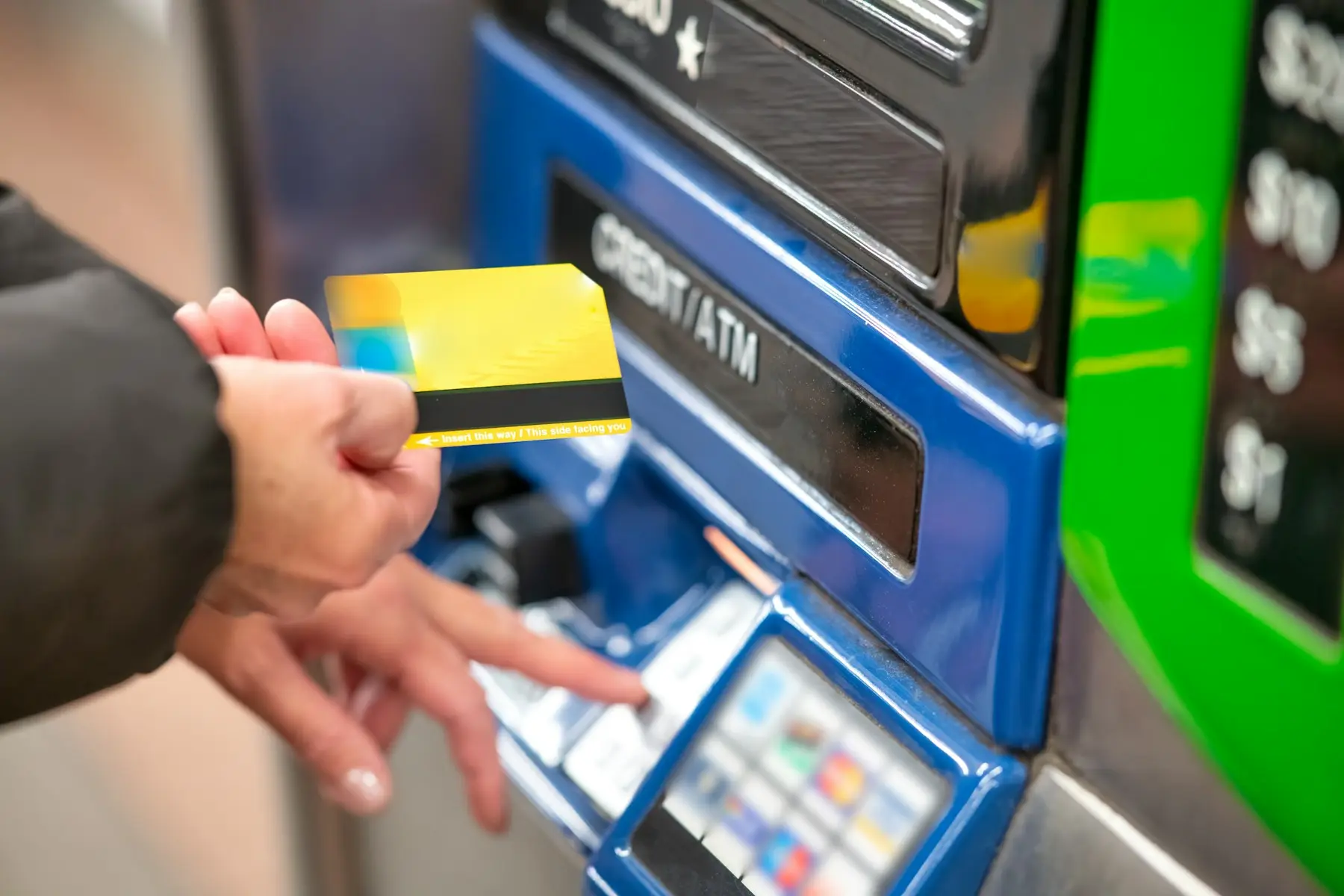 A hand holding a card next to the credit card slot on a self-service machine