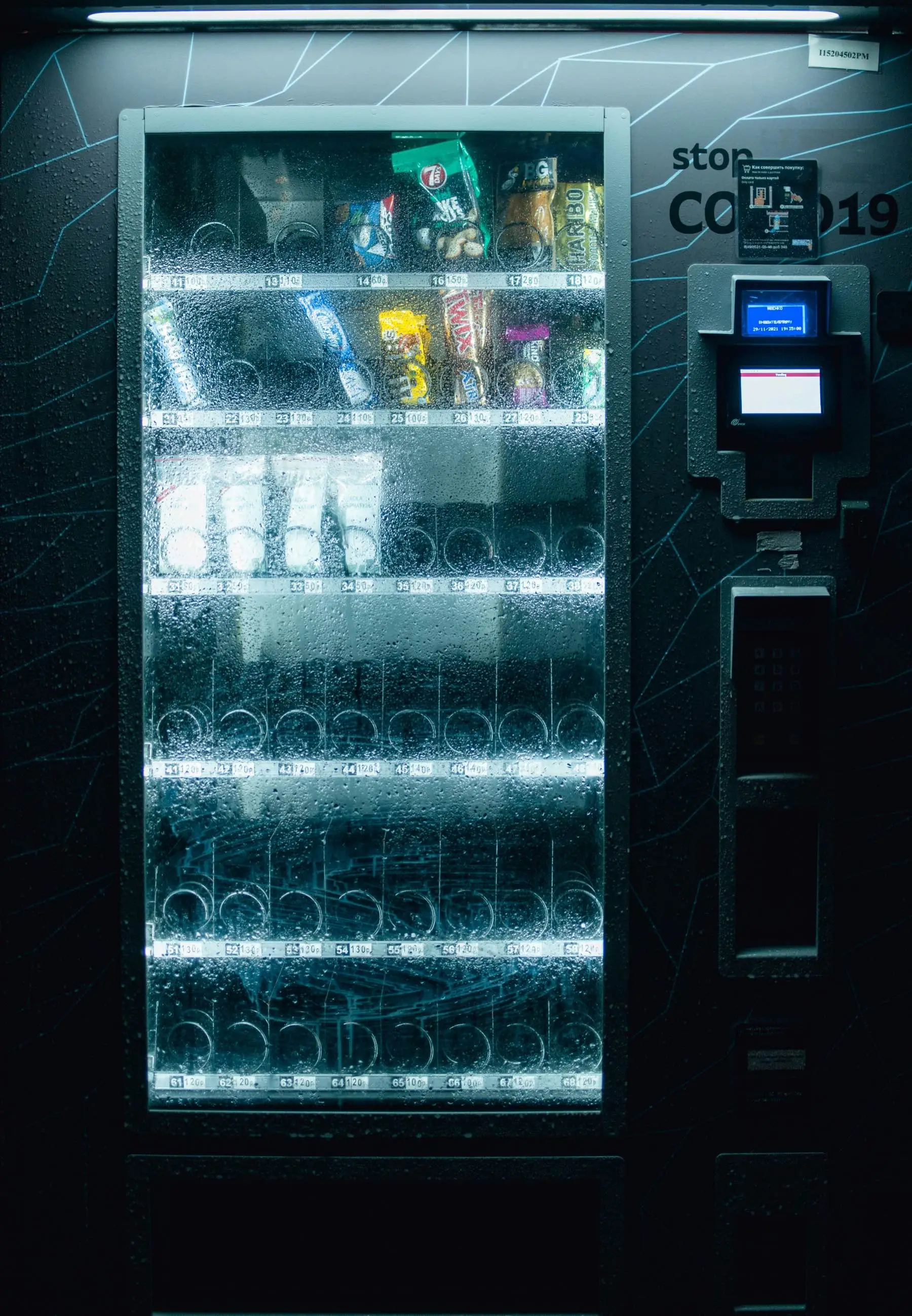 A snack vending machine at night with most of its spirals empty and a card reader beside the glass