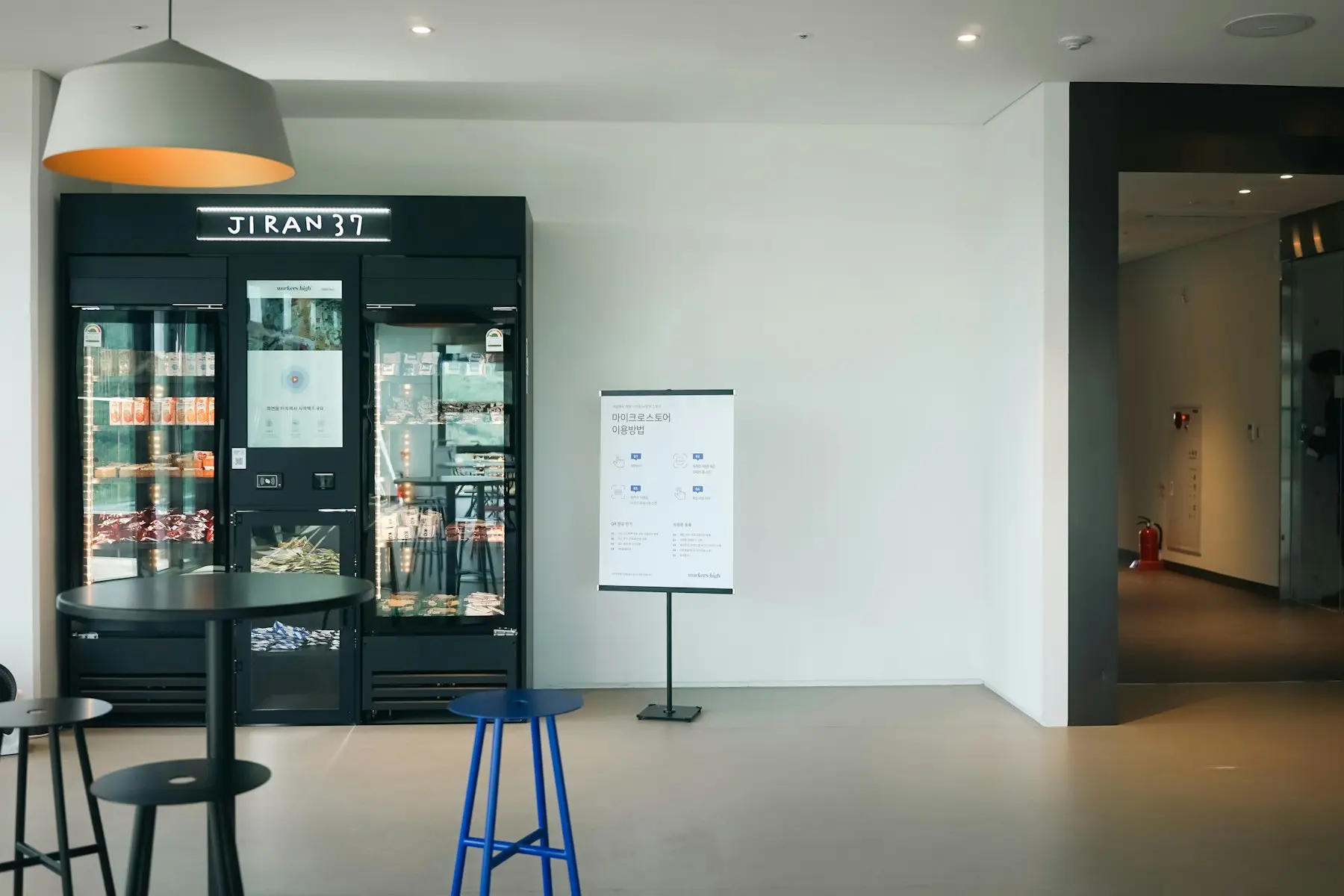 A break room with stools, a table, and a glass-door cooler